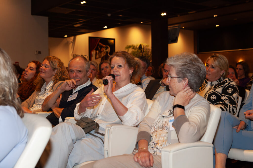 Congreszaal vol mensen waarvan een vrouw door een microfoon praat.