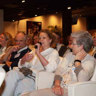 Congreszaal vol mensen waarvan een vrouw door een microfoon praat.