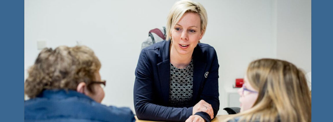 Vrouw aan tafel in gesprek met twee andere vrouwen.