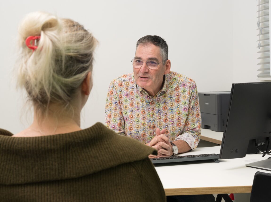 Huisarts zit achter zijn bureau en is in geeprek met een patient.