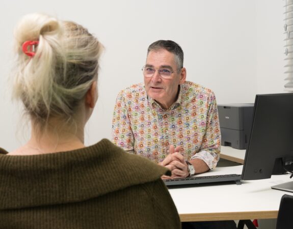 Huisarts zit achter zijn bureau en is in geeprek met een patient.